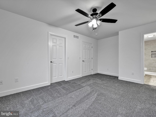 unfurnished bedroom with dark colored carpet, ensuite bathroom, and ceiling fan