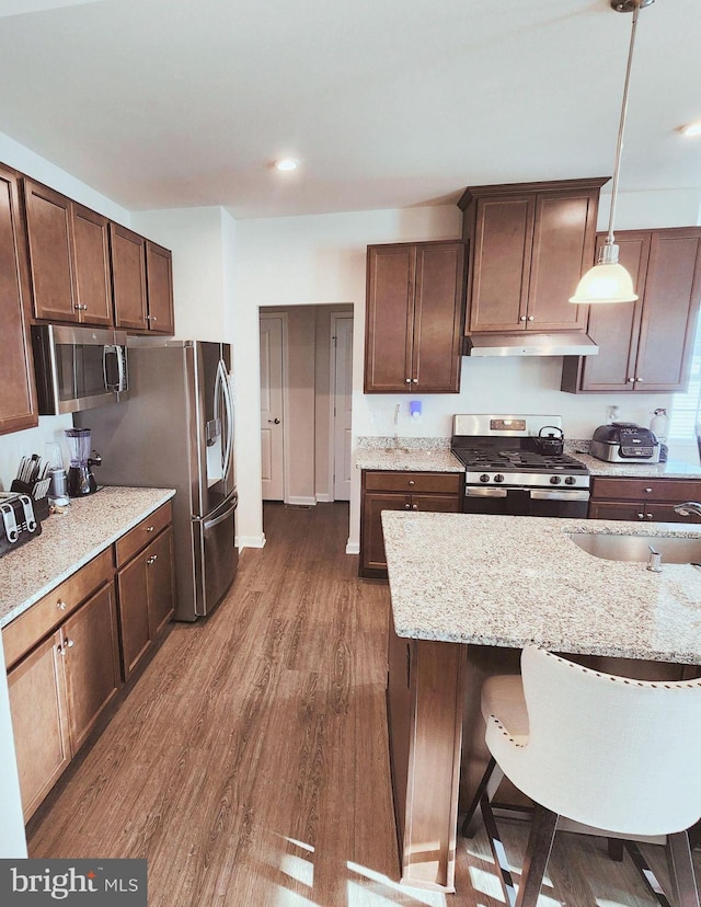 kitchen featuring appliances with stainless steel finishes, light stone counters, dark wood-type flooring, sink, and decorative light fixtures