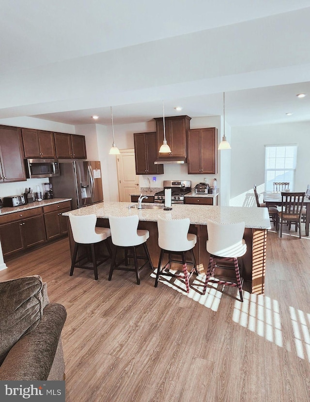 kitchen with light hardwood / wood-style flooring, an island with sink, decorative light fixtures, a kitchen bar, and appliances with stainless steel finishes