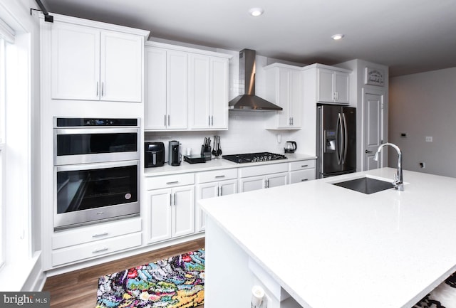 kitchen featuring appliances with stainless steel finishes, a kitchen island with sink, sink, wall chimney range hood, and white cabinets