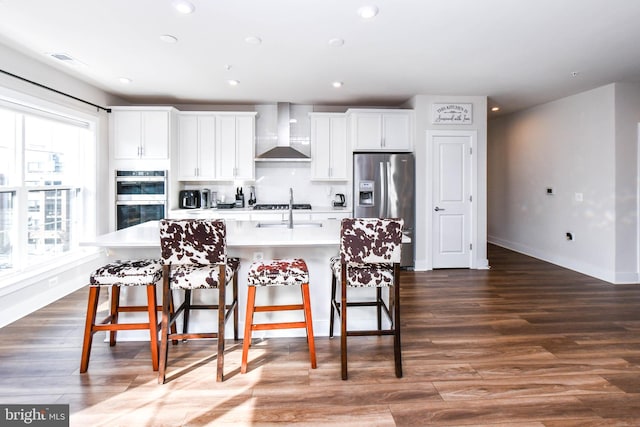 kitchen featuring white cabinets, an island with sink, wall chimney exhaust hood, and stainless steel appliances