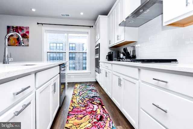 kitchen with white cabinetry, wall chimney range hood, gas cooktop, light stone counters, and dark hardwood / wood-style floors