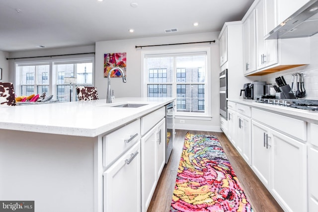 kitchen featuring sink, wall chimney exhaust hood, dark wood-type flooring, a center island with sink, and white cabinets