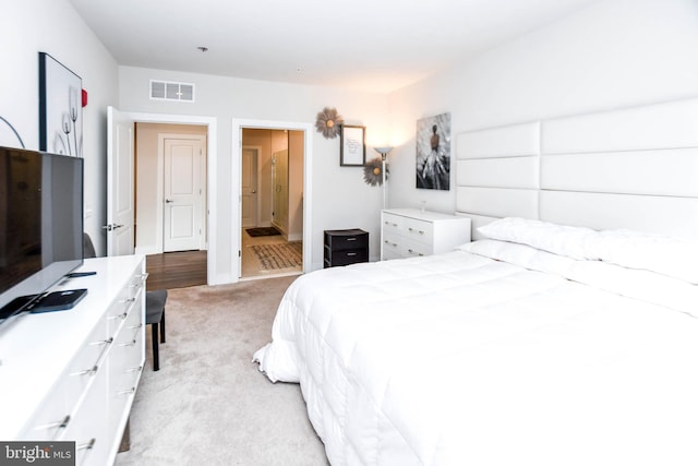 bedroom with ensuite bathroom and light colored carpet