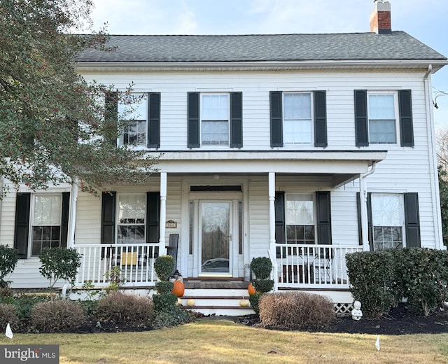 view of front of property featuring covered porch, a chimney, and roof with shingles