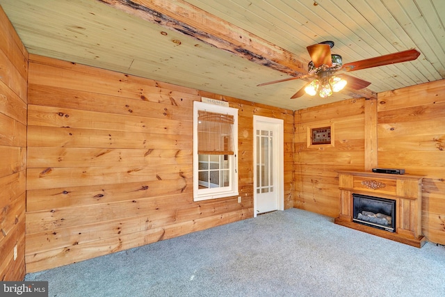 unfurnished living room featuring a glass covered fireplace, wooden walls, carpet flooring, and wood ceiling