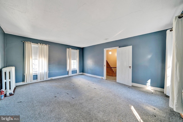 carpeted empty room with radiator heating unit and baseboards