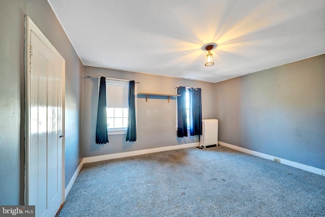 spare room featuring baseboards, radiator, and carpet