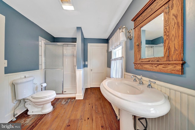 bathroom with a shower stall, toilet, a wainscoted wall, and wood-type flooring