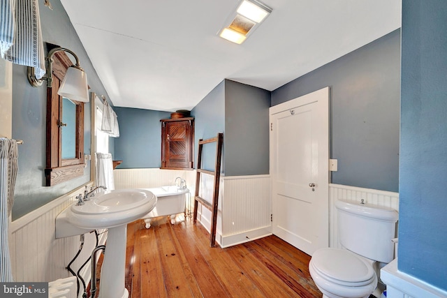 bathroom featuring toilet, a sink, a bathing tub, wood-type flooring, and wainscoting