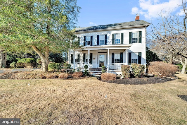 colonial inspired home featuring a front yard, a porch, and a chimney