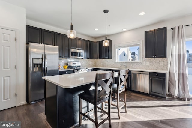 kitchen featuring hardwood / wood-style floors, appliances with stainless steel finishes, a center island, pendant lighting, and a kitchen bar