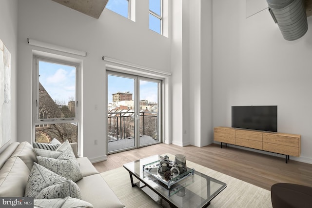 living area with a towering ceiling, baseboards, and wood finished floors