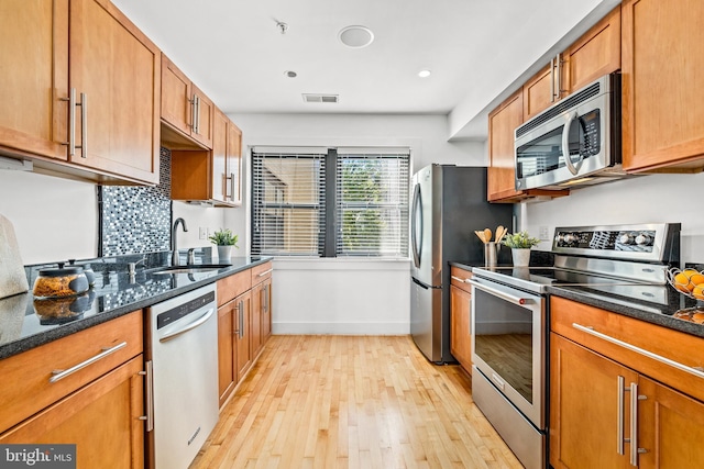 kitchen with stainless steel appliances, light hardwood / wood-style flooring, dark stone counters, and sink