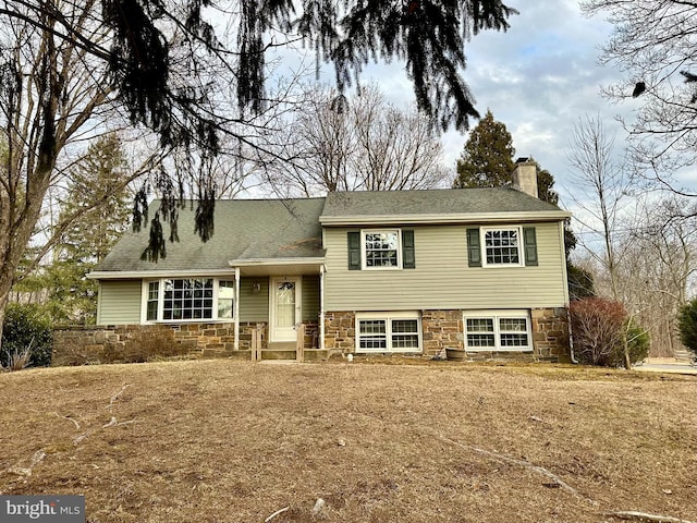 split level home with stone siding, a chimney, and roof with shingles