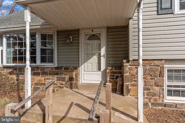 doorway to property featuring a shingled roof and stone siding