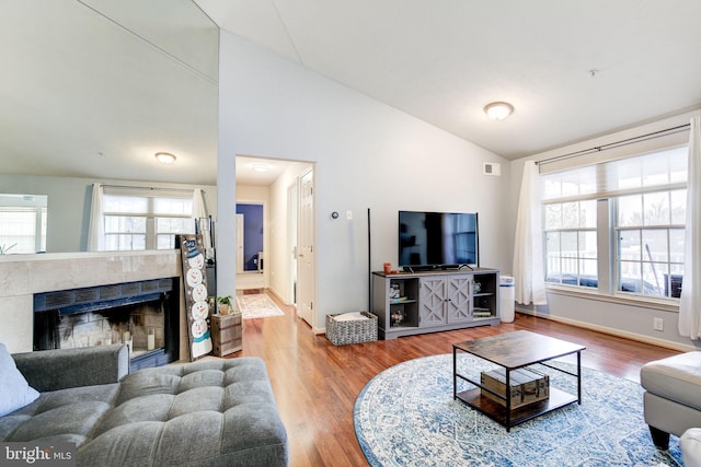 living room featuring wood-type flooring, lofted ceiling, and a tile fireplace