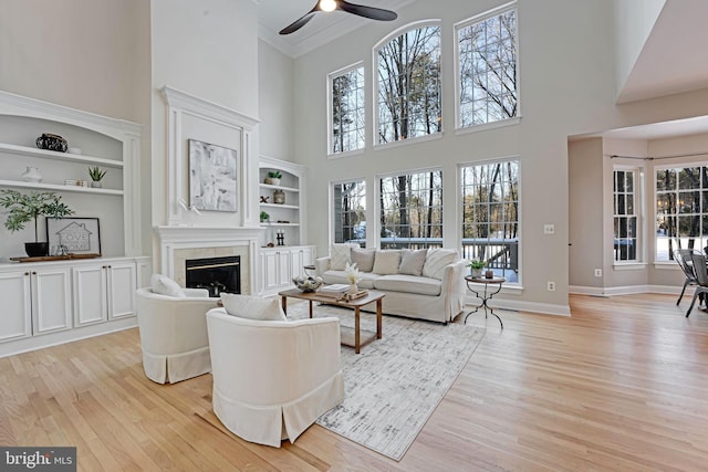 living room with ceiling fan, built in features, ornamental molding, and light hardwood / wood-style flooring