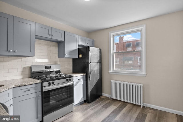 kitchen with black fridge, decorative backsplash, radiator heating unit, gray cabinets, and gas stove