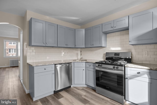 kitchen featuring stainless steel appliances, sink, light stone counters, radiator, and backsplash