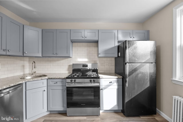 kitchen with light stone counters, radiator, light wood-type flooring, appliances with stainless steel finishes, and sink