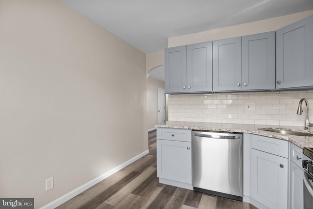 kitchen with light stone counters, stainless steel dishwasher, decorative backsplash, and sink