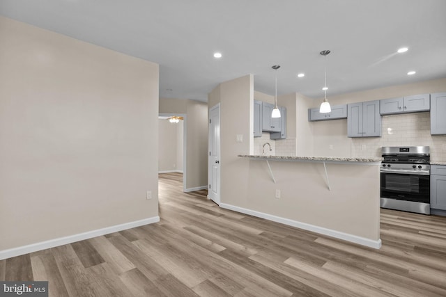 kitchen with gray cabinetry, light hardwood / wood-style flooring, stainless steel gas stove, and kitchen peninsula