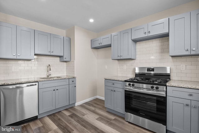 kitchen with light stone countertops, backsplash, dark hardwood / wood-style flooring, appliances with stainless steel finishes, and sink