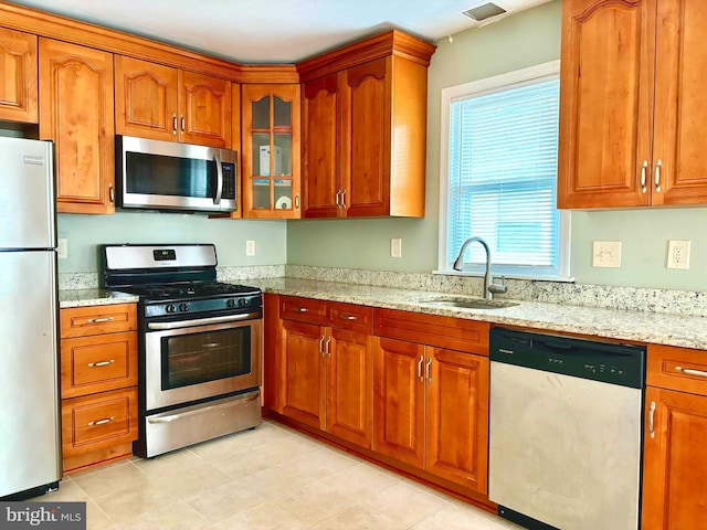 kitchen featuring stainless steel appliances, light stone counters, and sink