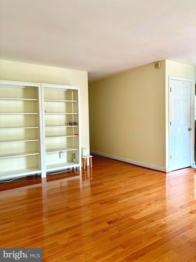 empty room featuring built in shelves and light hardwood / wood-style floors