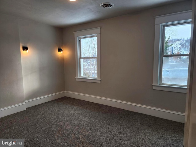 empty room with dark colored carpet and a healthy amount of sunlight