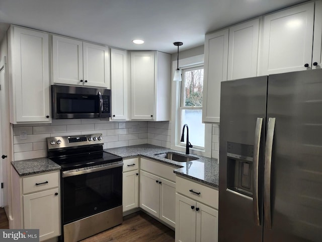 kitchen with stainless steel appliances, white cabinetry, dark stone countertops, and sink