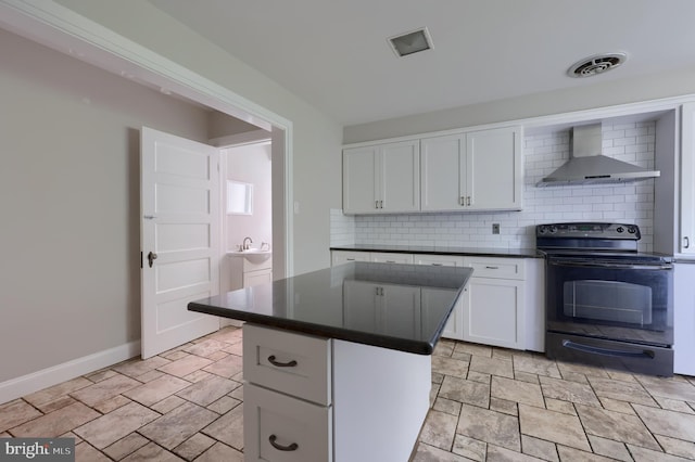 kitchen featuring decorative backsplash, wall chimney range hood, white cabinets, a center island, and black range with electric stovetop