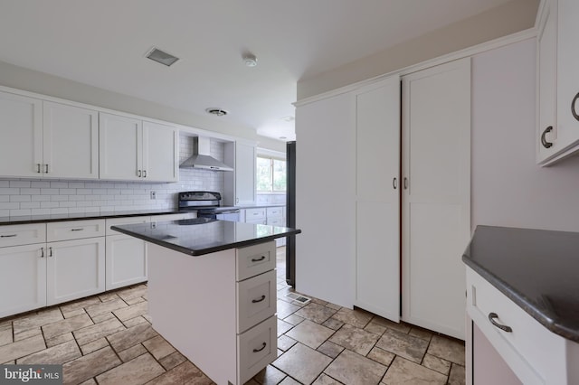 kitchen with a center island, white cabinets, electric stove, wall chimney range hood, and tasteful backsplash