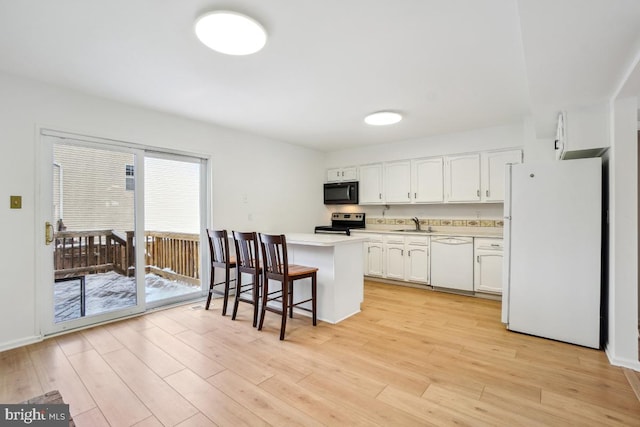 kitchen with white appliances, a breakfast bar area, light hardwood / wood-style floors, white cabinets, and sink