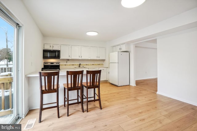 kitchen with light wood-type flooring, white cabinets, stainless steel electric range oven, white refrigerator, and a kitchen breakfast bar