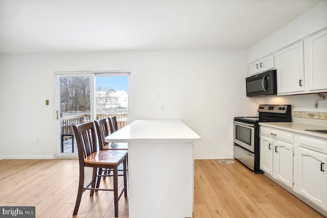 kitchen with white cabinets, light wood-type flooring, stainless steel electric range, and a breakfast bar area