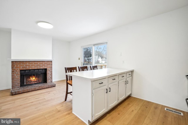 kitchen with kitchen peninsula, a breakfast bar, a brick fireplace, white cabinets, and light hardwood / wood-style flooring