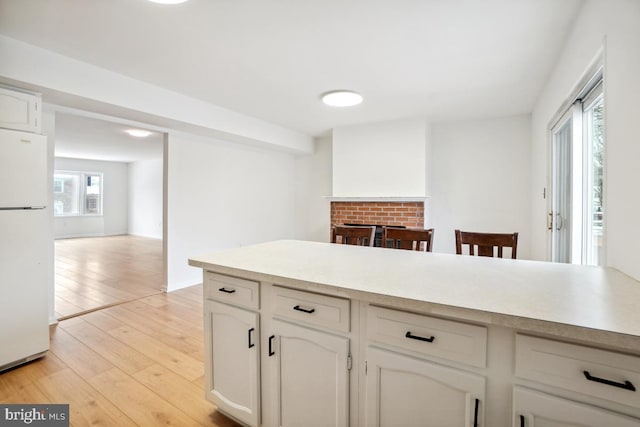 kitchen with white fridge, white cabinets, light wood-type flooring, and a fireplace