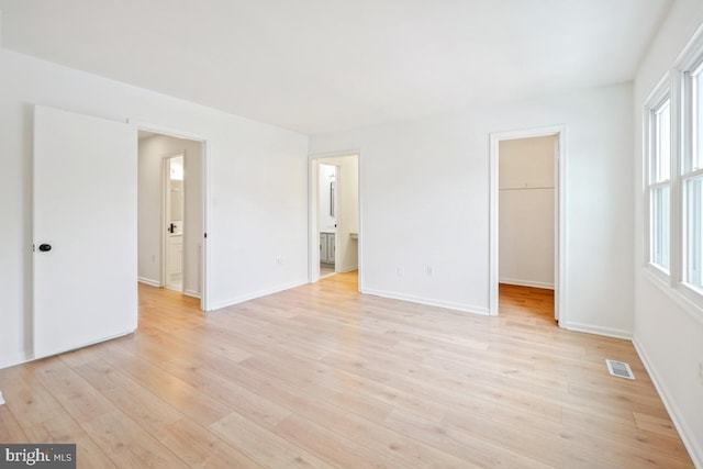 unfurnished bedroom with light hardwood / wood-style flooring, a spacious closet, a closet, multiple windows, and connected bathroom