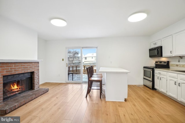 kitchen featuring stainless steel electric stove, light wood-type flooring, a breakfast bar, a fireplace, and white cabinets