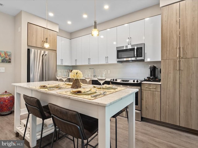 kitchen featuring appliances with stainless steel finishes, tasteful backsplash, white cabinets, light wood-type flooring, and a breakfast bar area