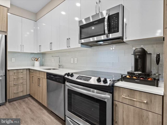 kitchen featuring white cabinetry, stainless steel appliances, decorative backsplash, sink, and light wood-type flooring