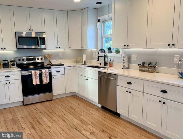 kitchen featuring stainless steel appliances, white cabinetry, light wood-type flooring, and pendant lighting