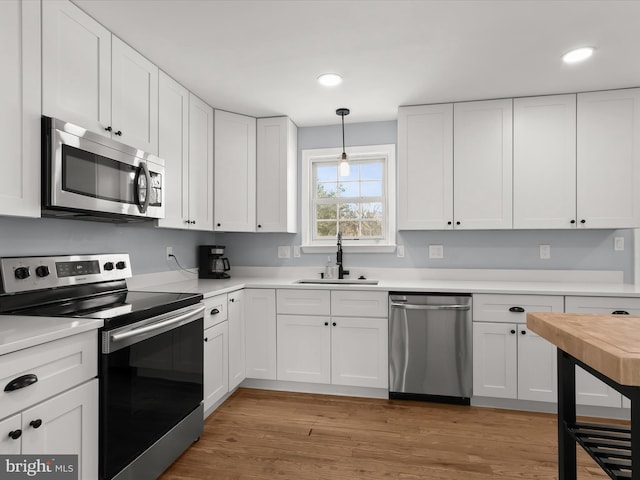 kitchen with sink, stainless steel appliances, white cabinets, and hanging light fixtures