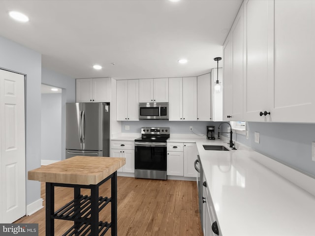 kitchen with decorative light fixtures, stainless steel appliances, light wood-type flooring, white cabinetry, and sink