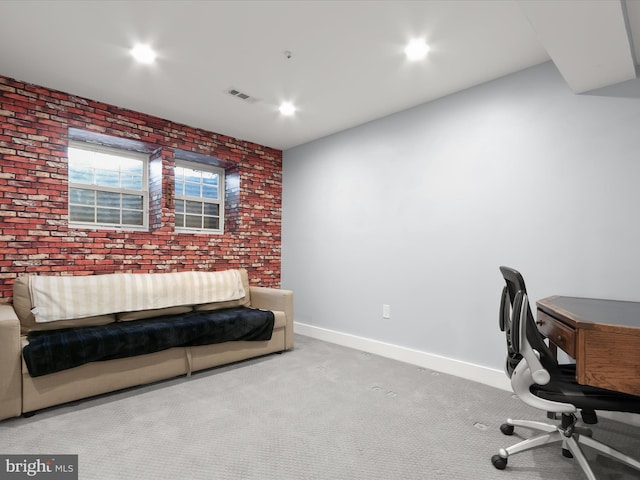 carpeted home office featuring brick wall