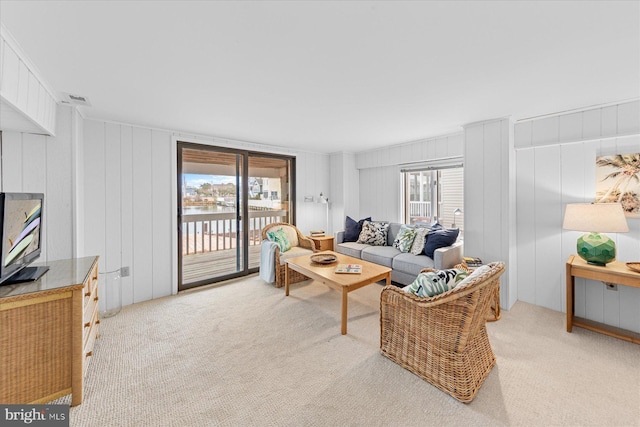 living room featuring plenty of natural light, light colored carpet, and wooden walls