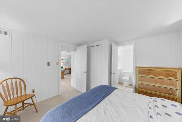 carpeted bedroom featuring ensuite bathroom, a closet, and wood walls