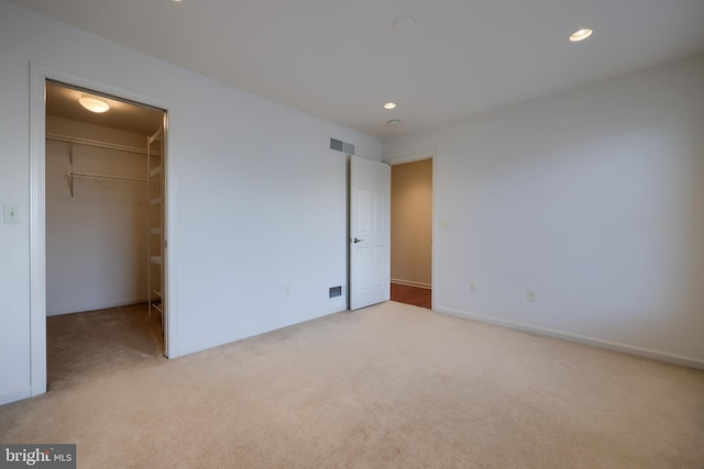 unfurnished bedroom with light colored carpet, a walk in closet, and a closet